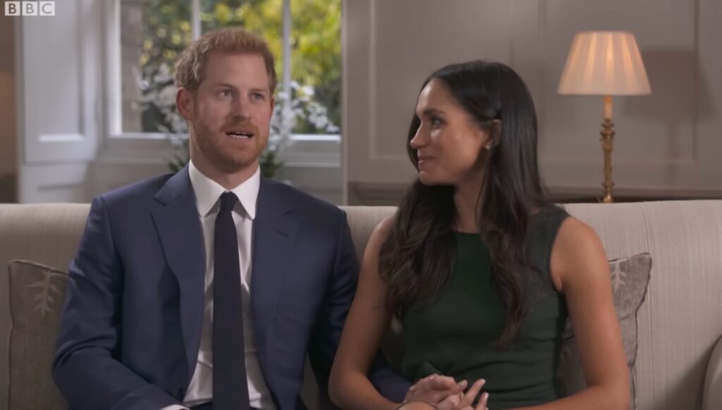 Prince Harry talking as Meghan Markle looks at him during engagement interview