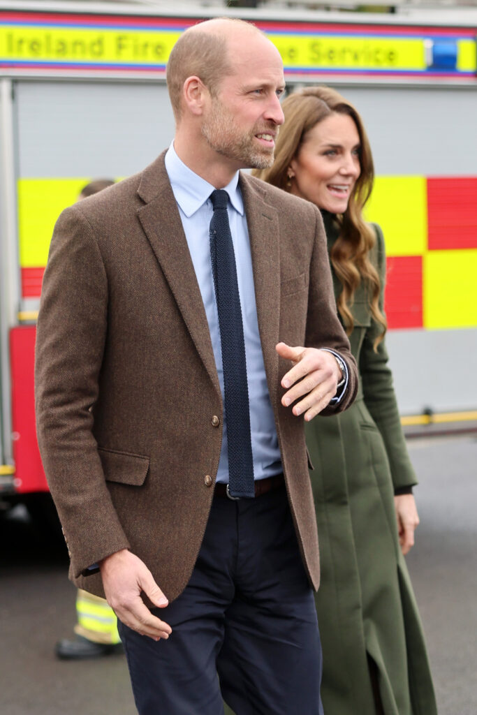 Prince William with a serious expression walking with Princess Kate behind him