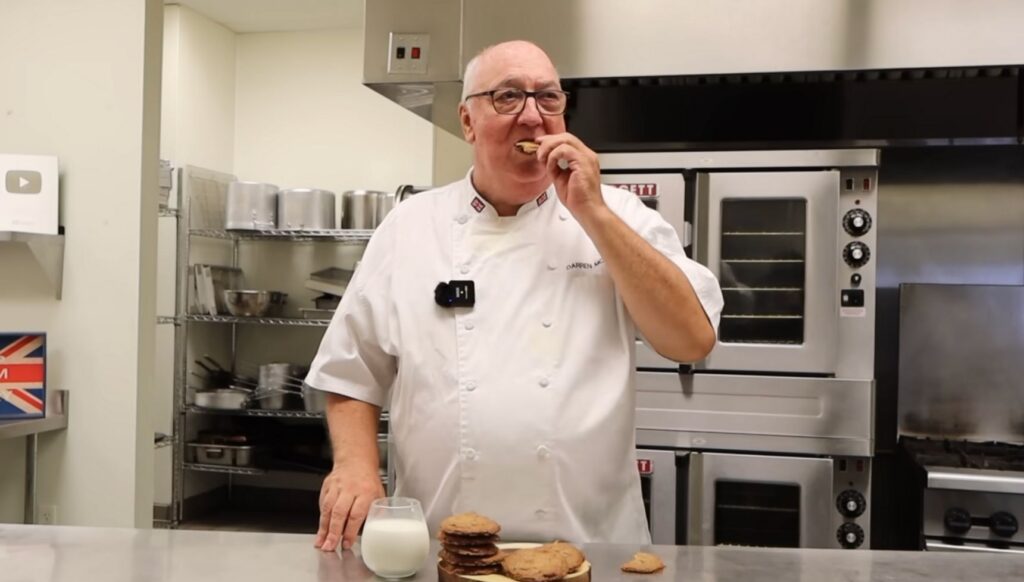 Darren McGrady's in a professional kitchen eating cookies with a glass of milk