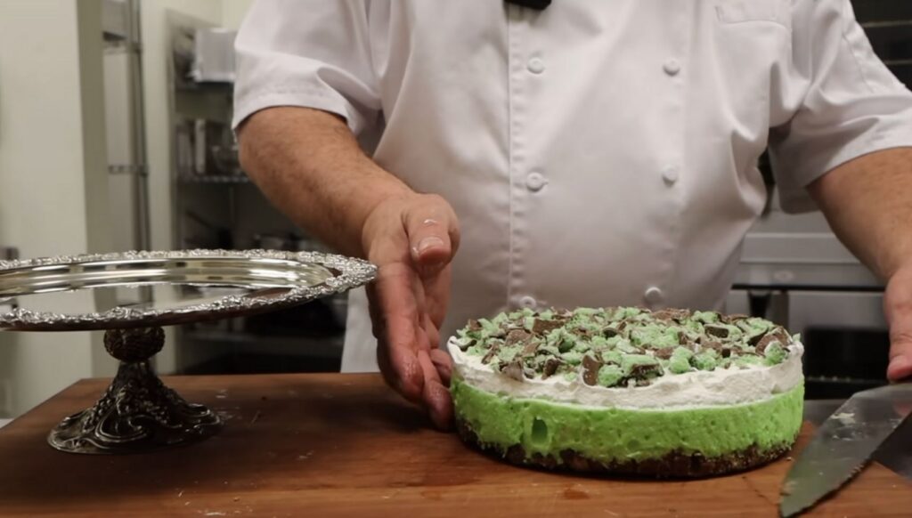 Darren McGrady lifting a green mint and chocolate cheese cake onto a platter