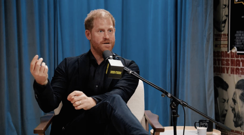 Prince Harry with his legs crossed over his knee and hand in air on podcast