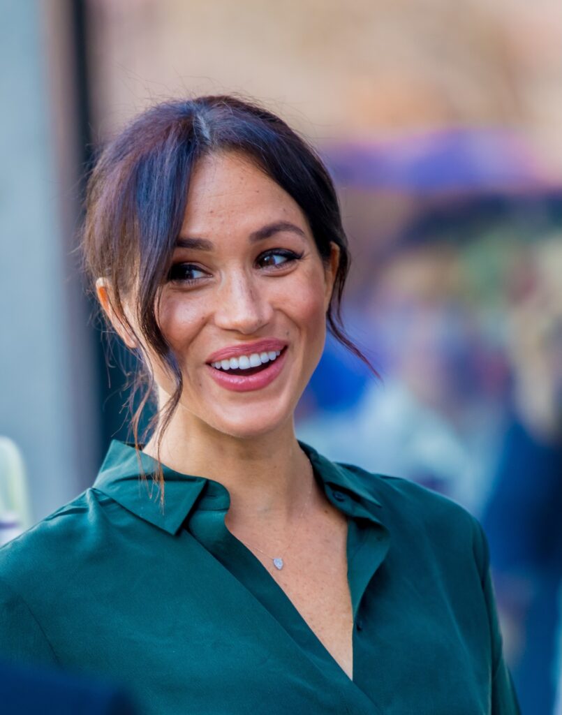 Meghan Markle smiling in green shirt with hair tied back