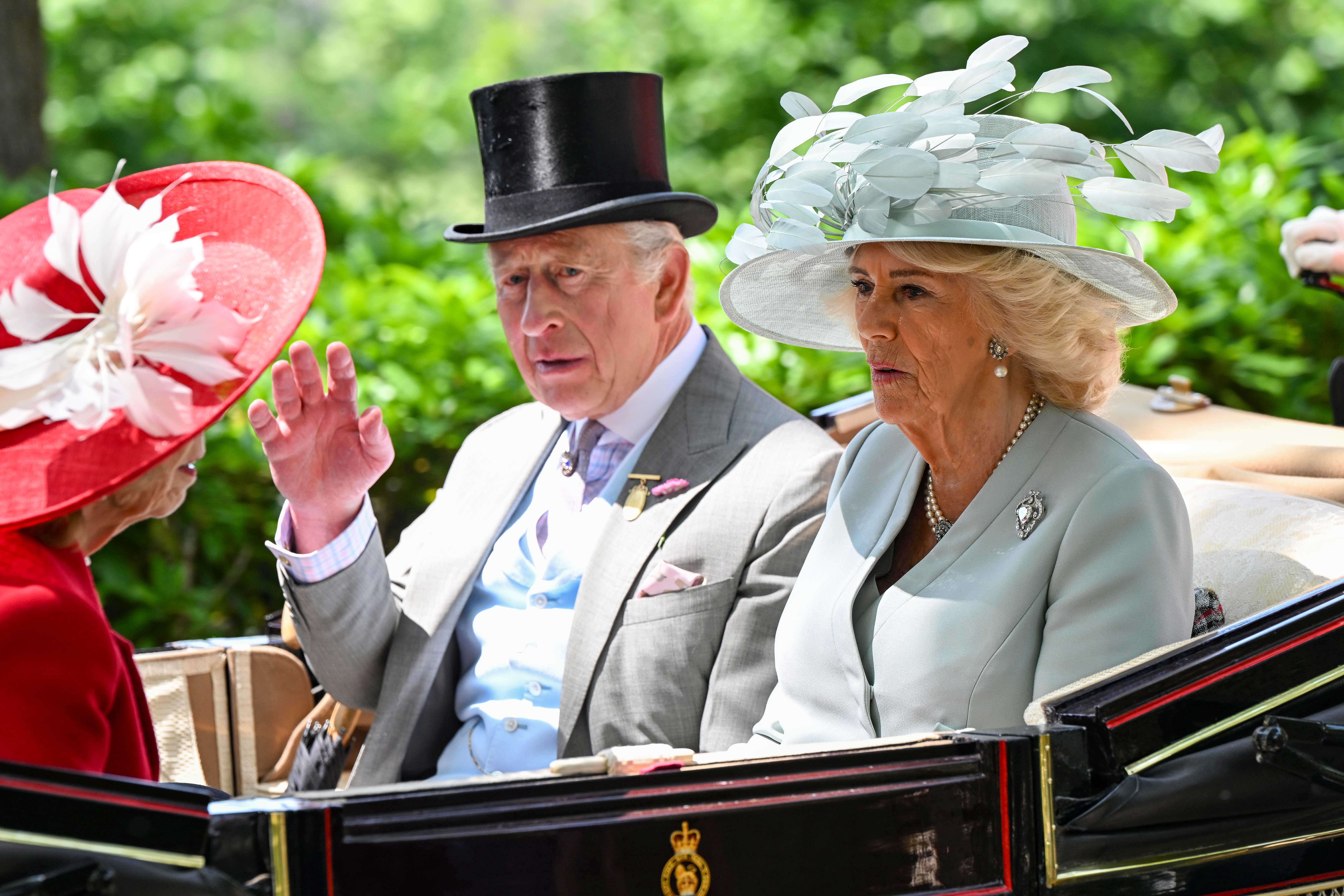 King Charles waving alongside Queen Camilla in a carriage