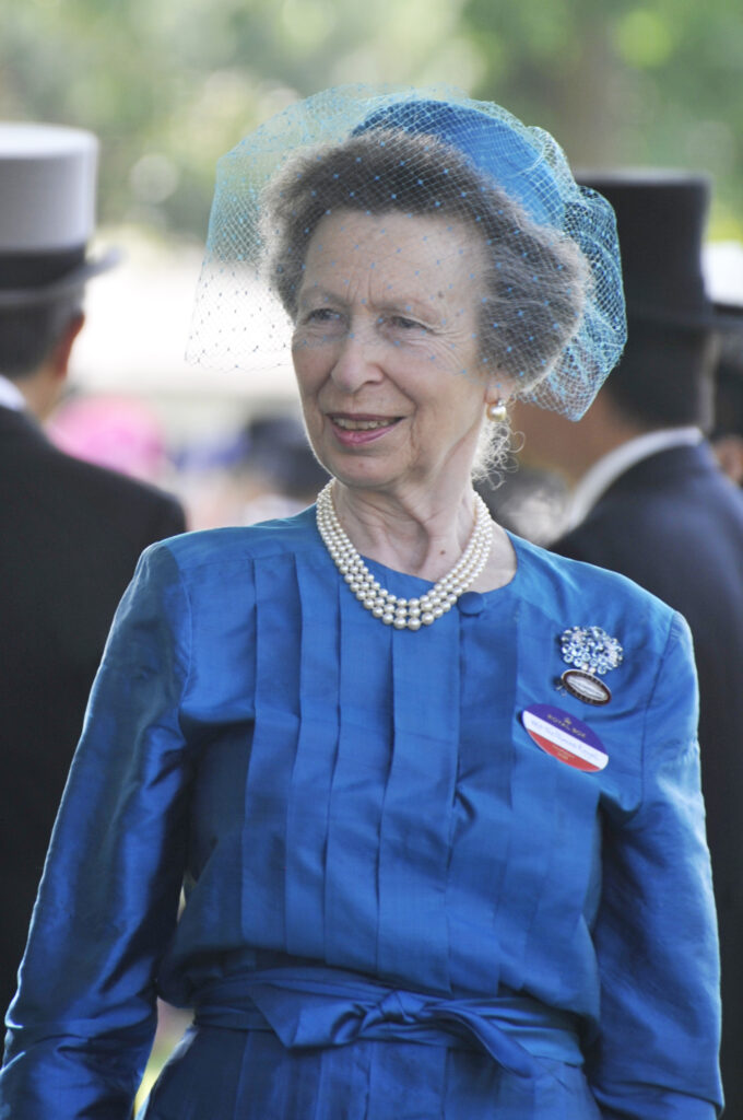 Princess Anne smiling wearing a blue hat, veil and dress