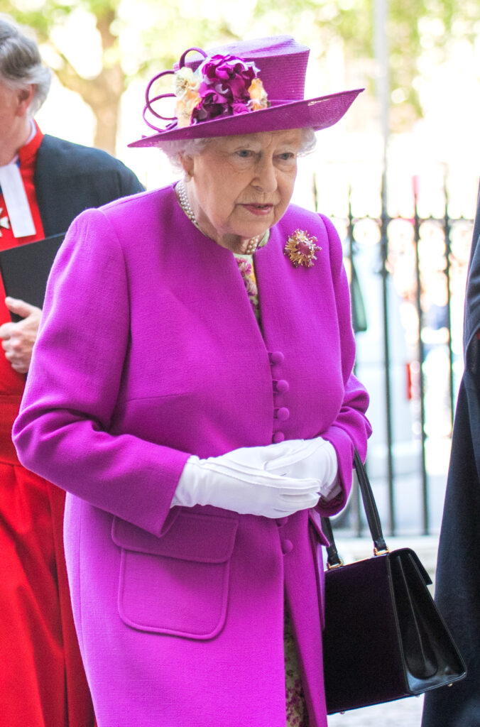 Queen Elizabeth II in a purple/pink outfit and hat 