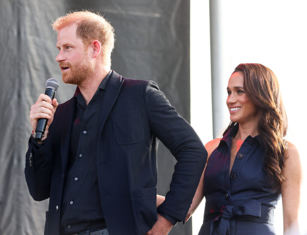 Prince Harry speaks into a microphone next to Meghan Sussex