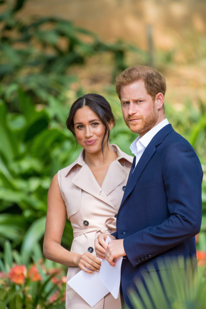 Meghan Markle smiling beside a frowning Prince Harry