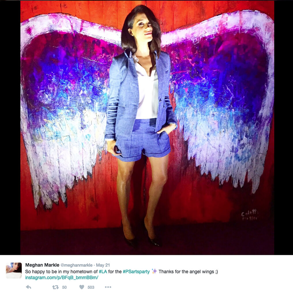 Meghan Markle posing in front of an angel wing mural 