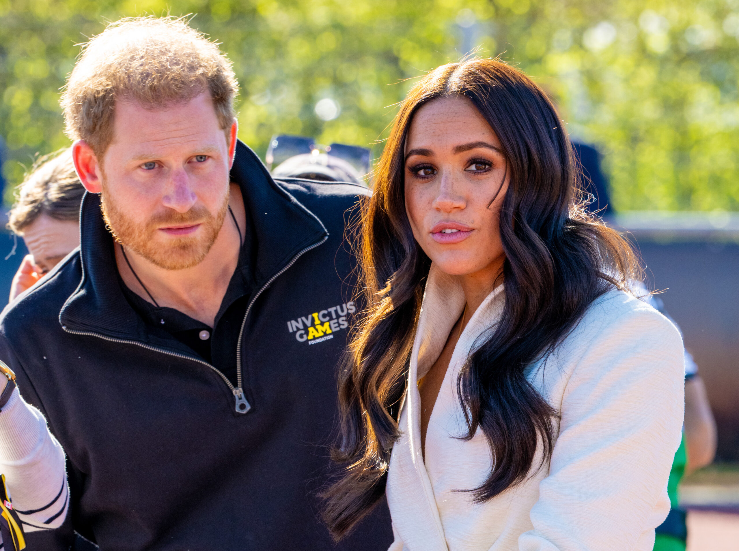 Prince Harry with a serious expression beside a frowning Meghan Markle