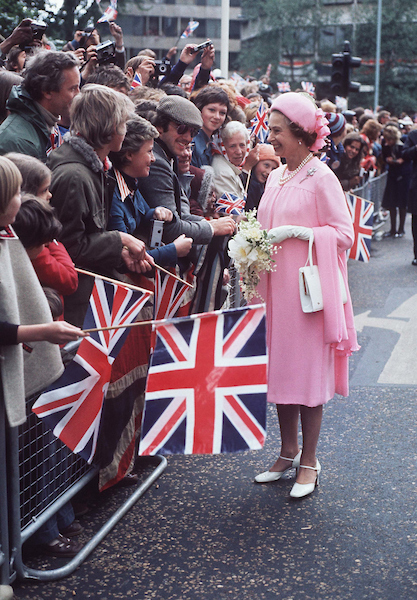 Queen Elizabeth II in a pink outfit greeting fans holding GB flags