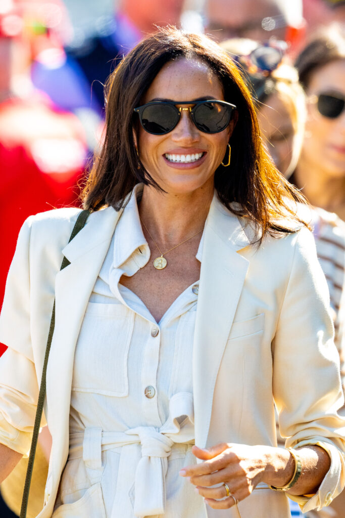 Meghan Markle smiling wearing sunglasses and a cream suuit
