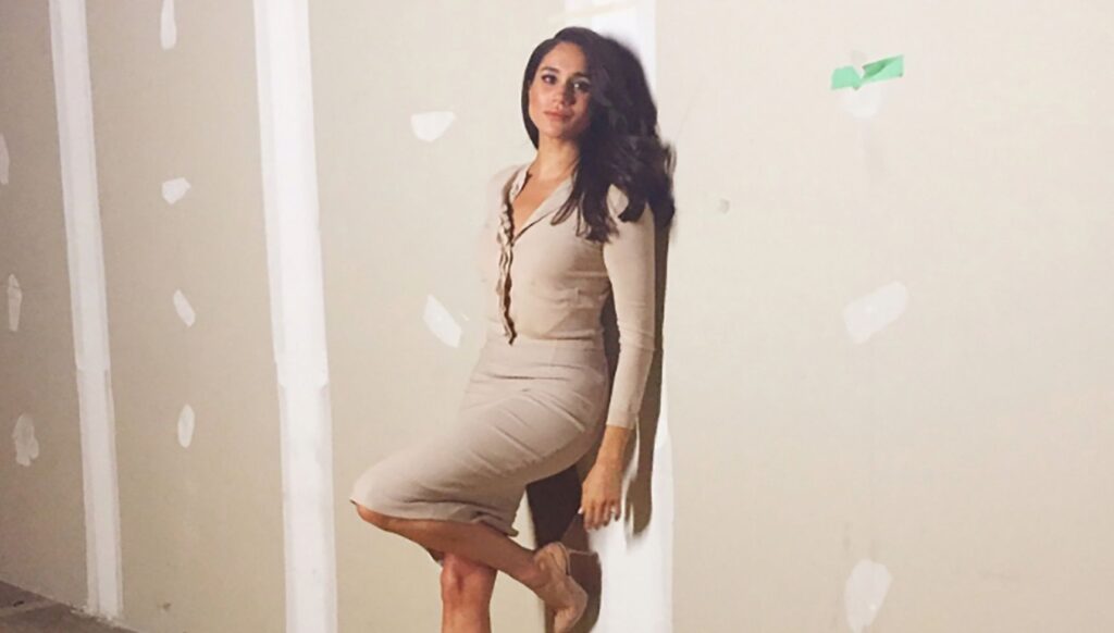 Meghan Markle posing in a cream dress against a wall