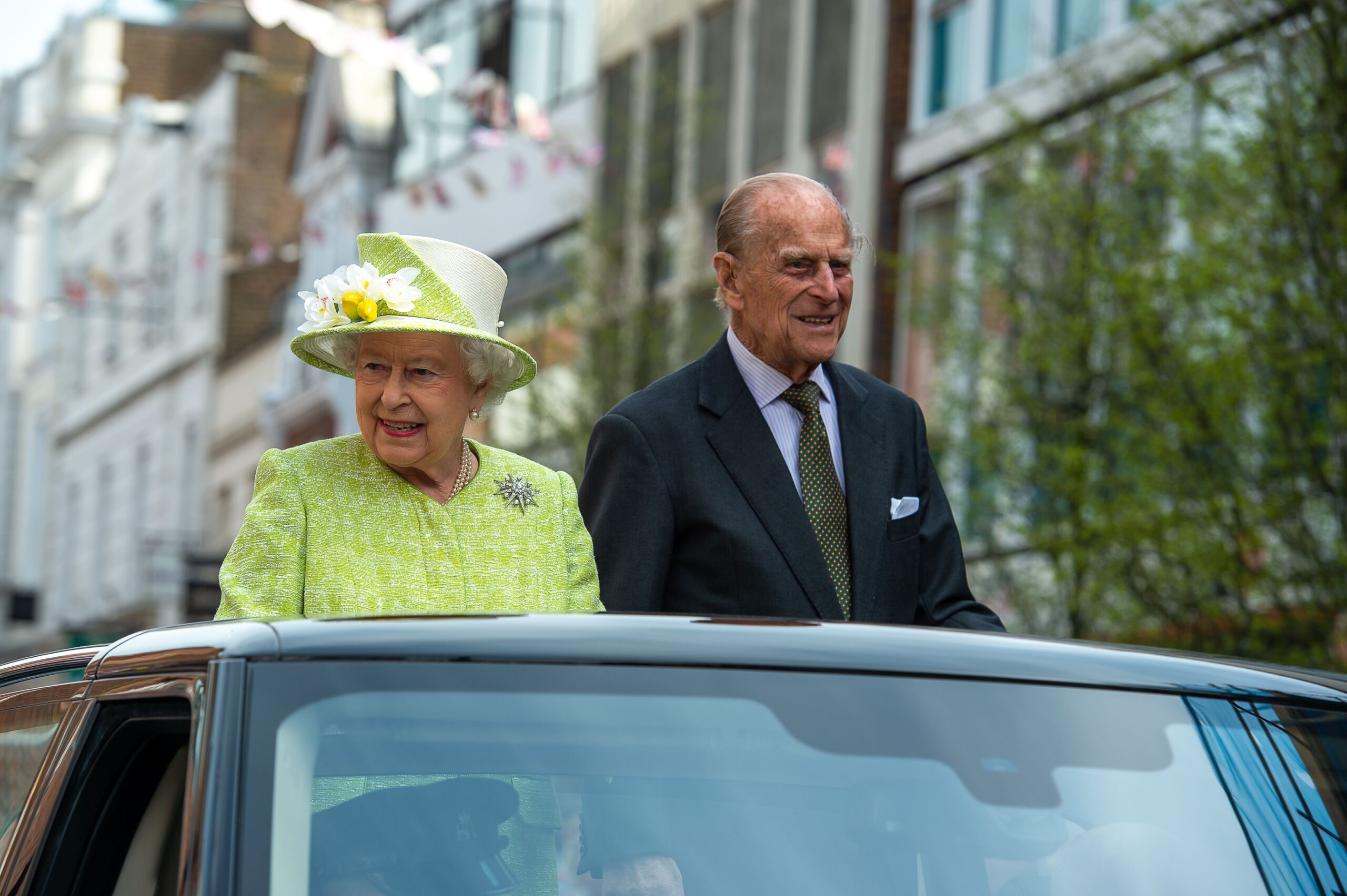 Queen Elizabeth and Prince Philip riding in an open top car waving to crowds