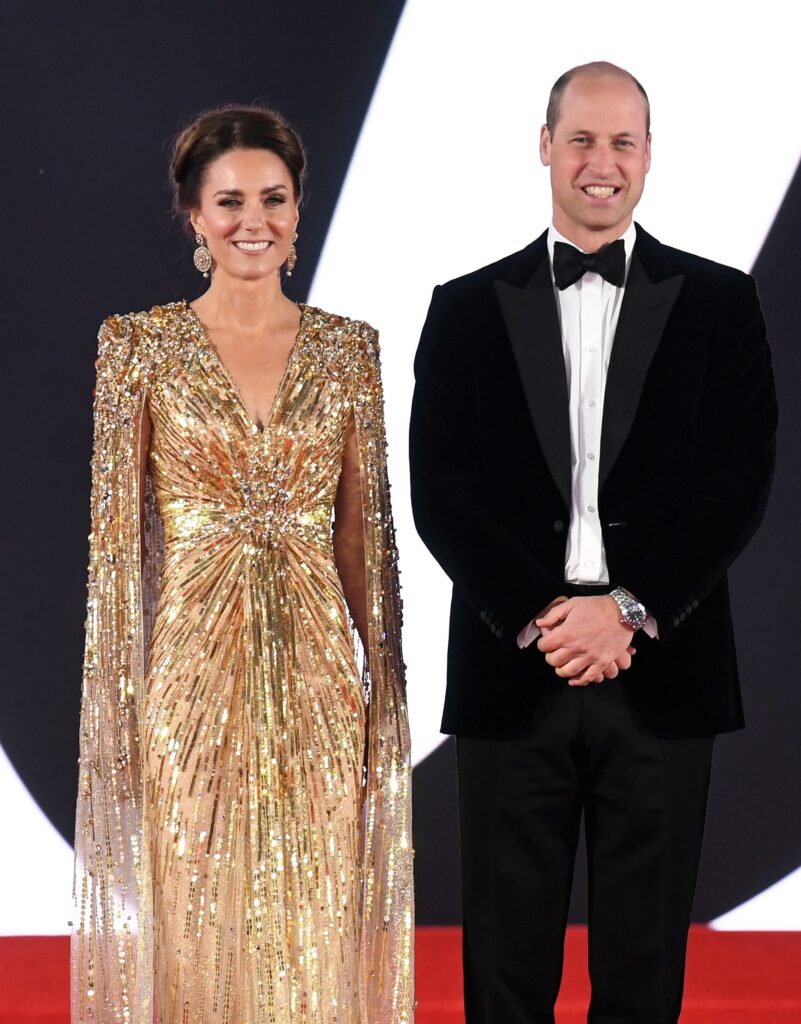 Princess Kate wearing a sparkling gold gown beside Prince William wearing a tuxedo at the No Time to Die premiere in 2021