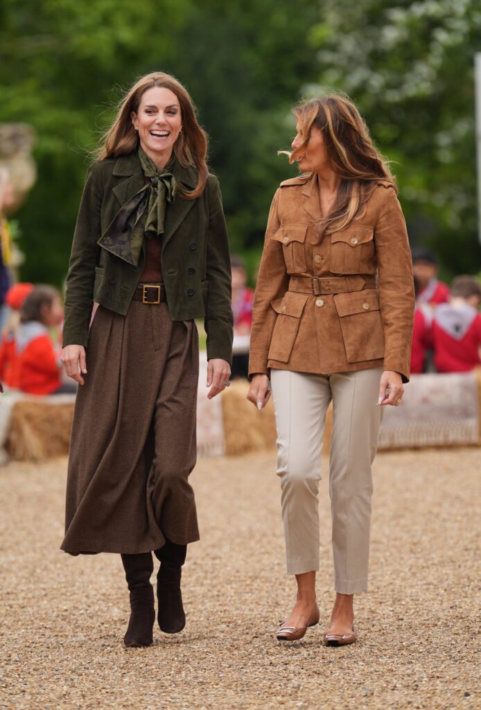 Princess Kate and First Lady Melania Trump walking in Frogmore gardens, Kate wears a green jacket and a long tweed skirt with brown boots whilst Melania wears cream trousers and a camel, suede jacket