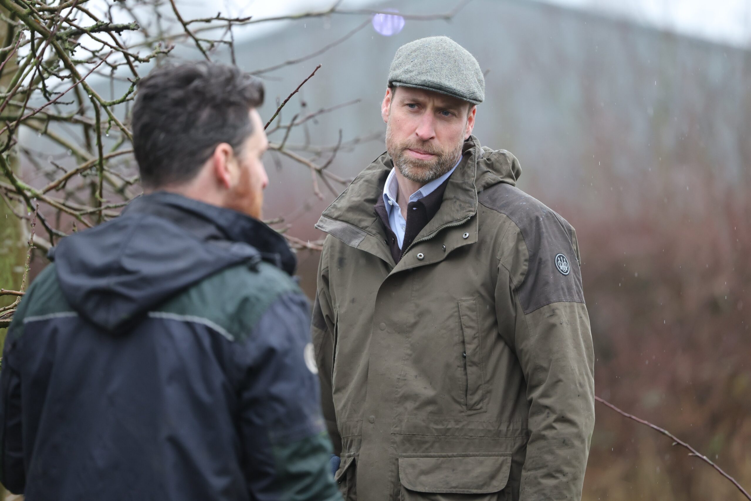Prince William frowning as he wears a flat cap whilst talking to someone