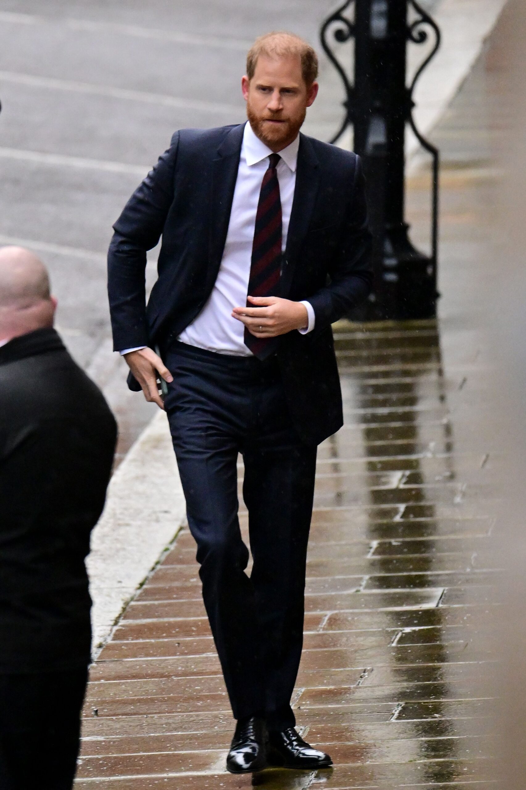 Prince Harry frowning, walking, wearing a blue suit