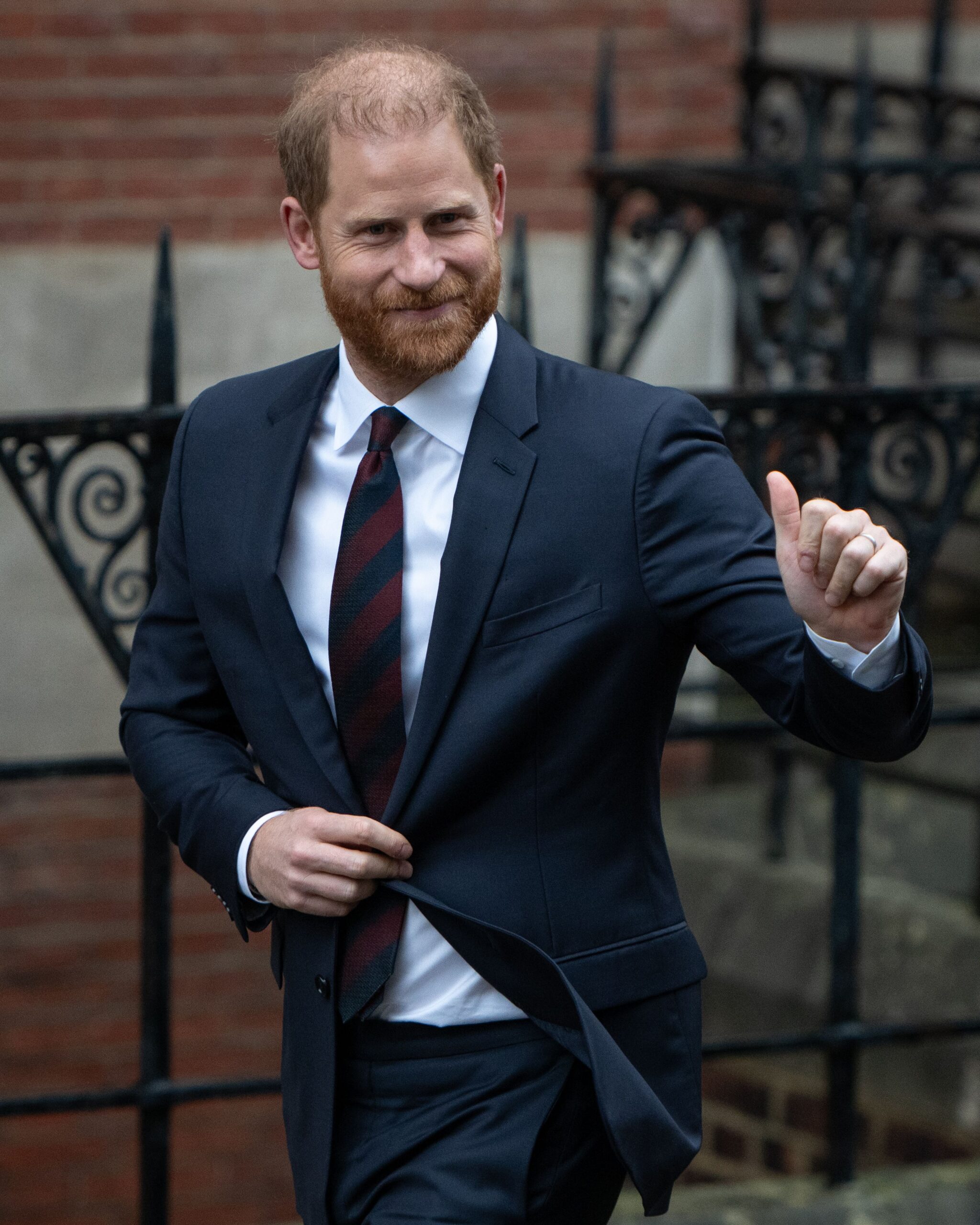 Prince Harry waving and smiling wearing a blue suit