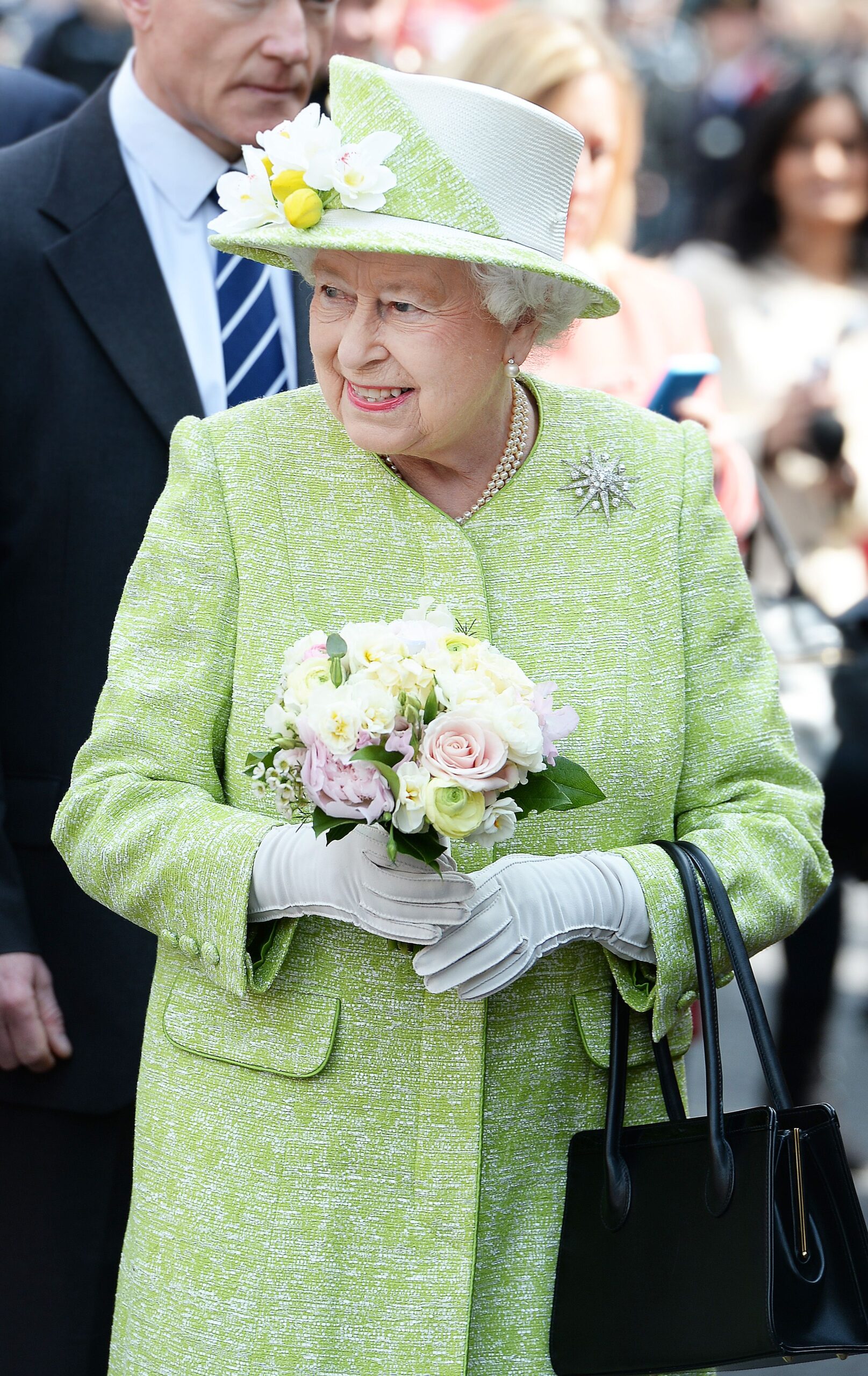 Queen Elizabeth smiling holding flowers wearing a green dress coat in 2016