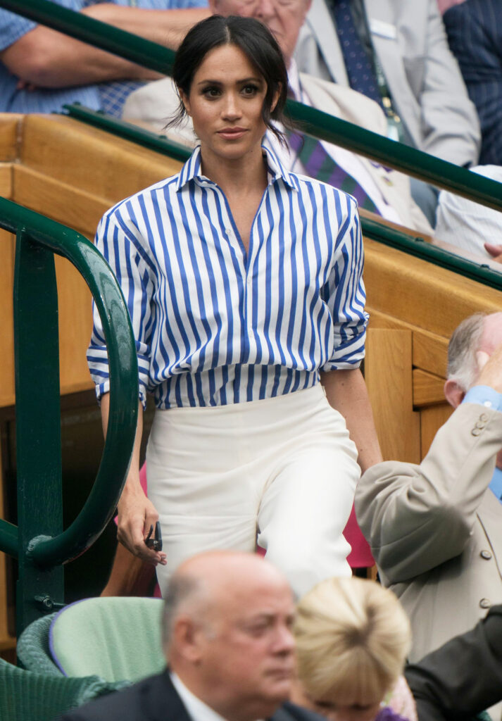 Meghan Markle wearing a blue and white striped shirt and cream trousers at Wimbledon in 2018