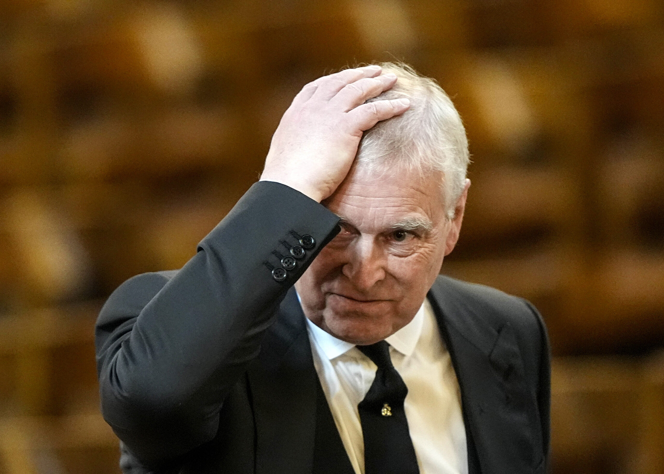 Andrew Mountbatten-Windsor frowning as he holds his head