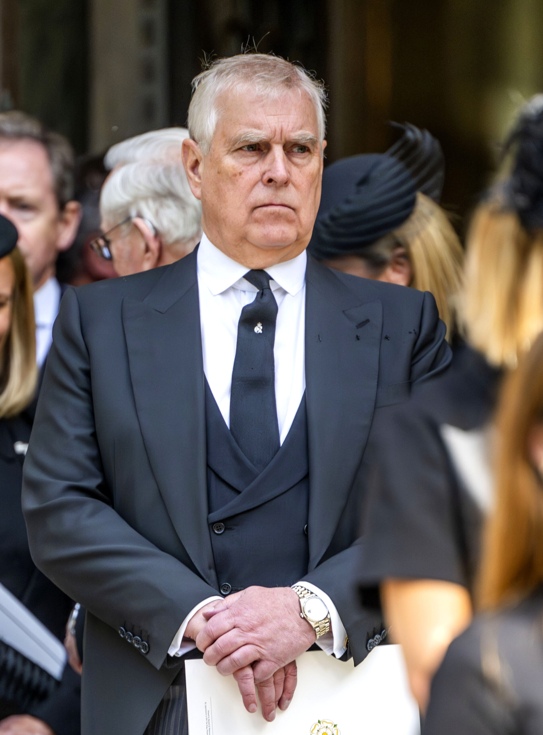 Andrew Mountbatten-Windsor frowning wearing a black tie and suit