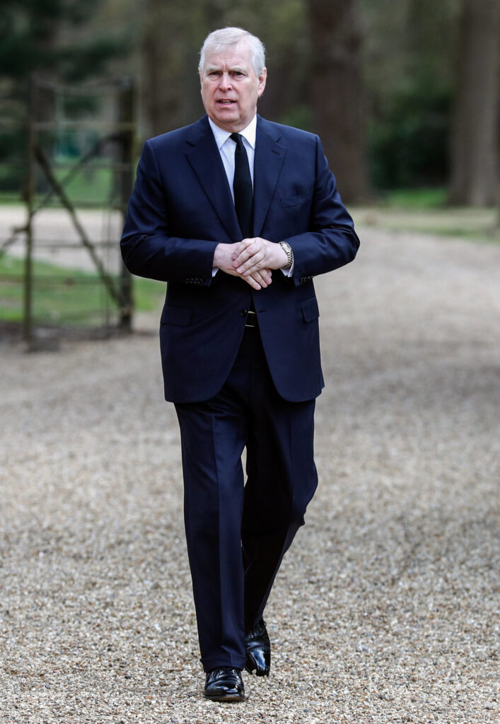 Andrew Mountbatten-Windsor clasping his hands, walking, wearing a navy suit