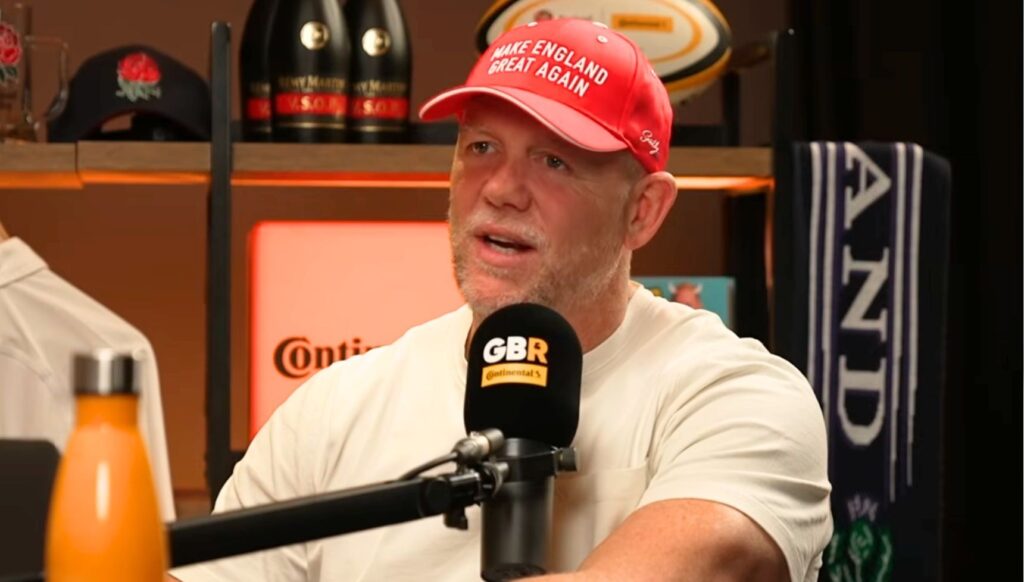 Mike Tindall talking into a podcast mic wearing a red Make England Great Again cap 