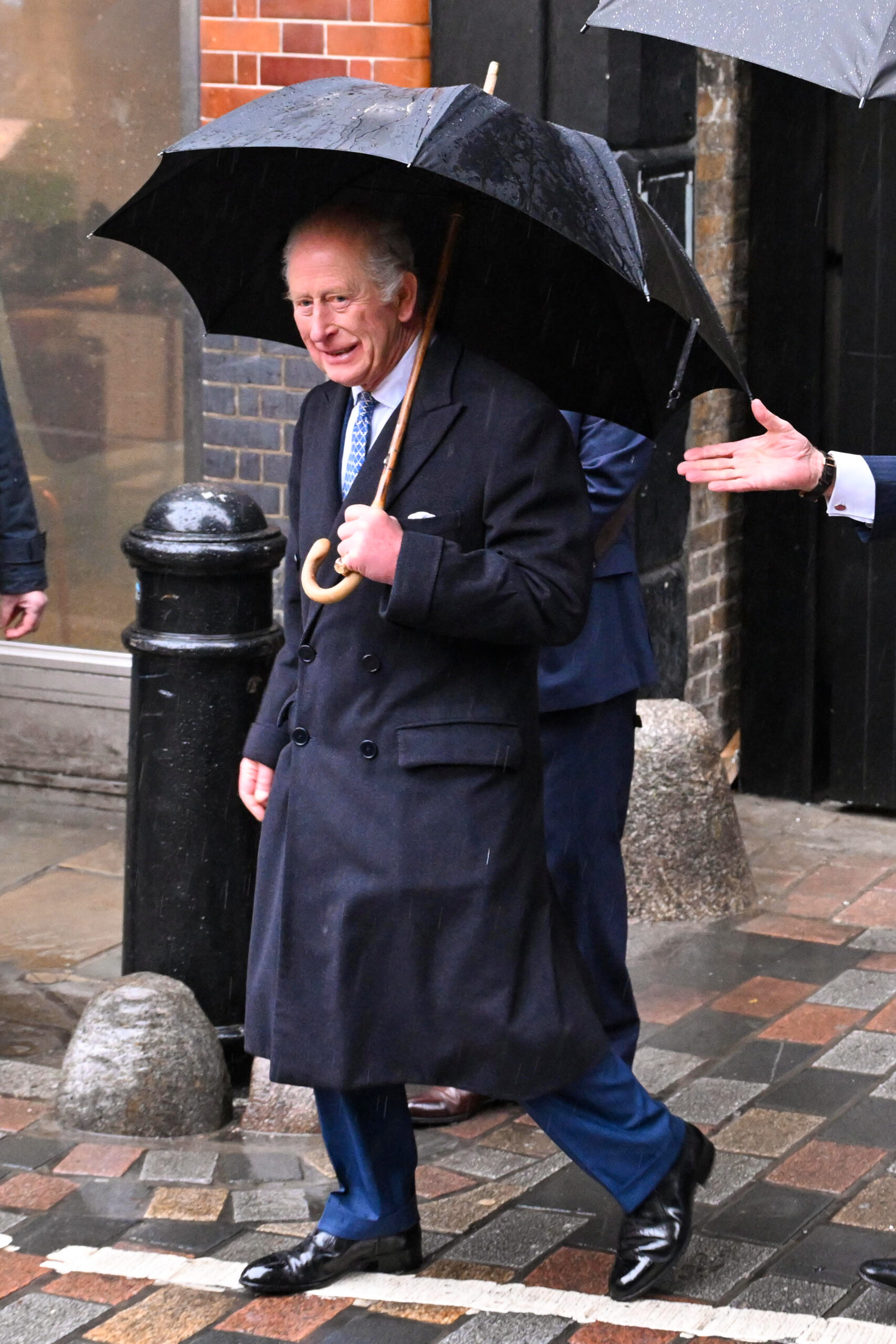 King Charles in a big coat and umbrella