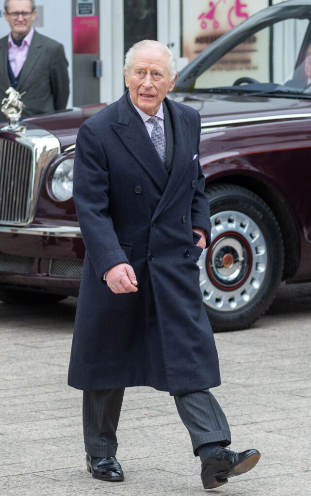 King Charles walking wearing a long navy coat