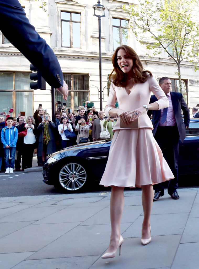 Princess Kate in a pastel pink skirt dress with a peplum waist, she smiles as she walks forward to greet someone
