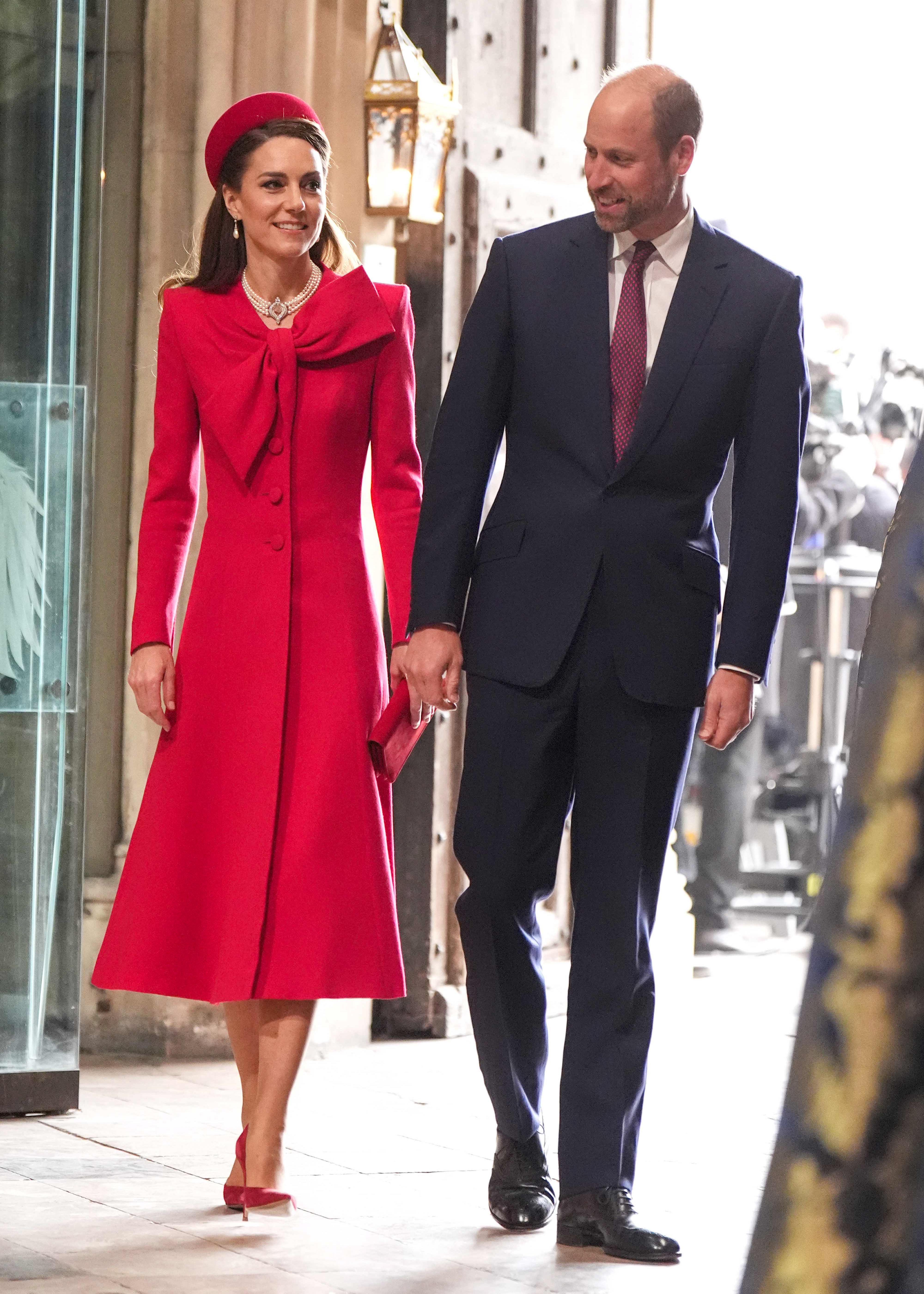 Princess Kate wearing a red outfit beside Prince William wearing a suit