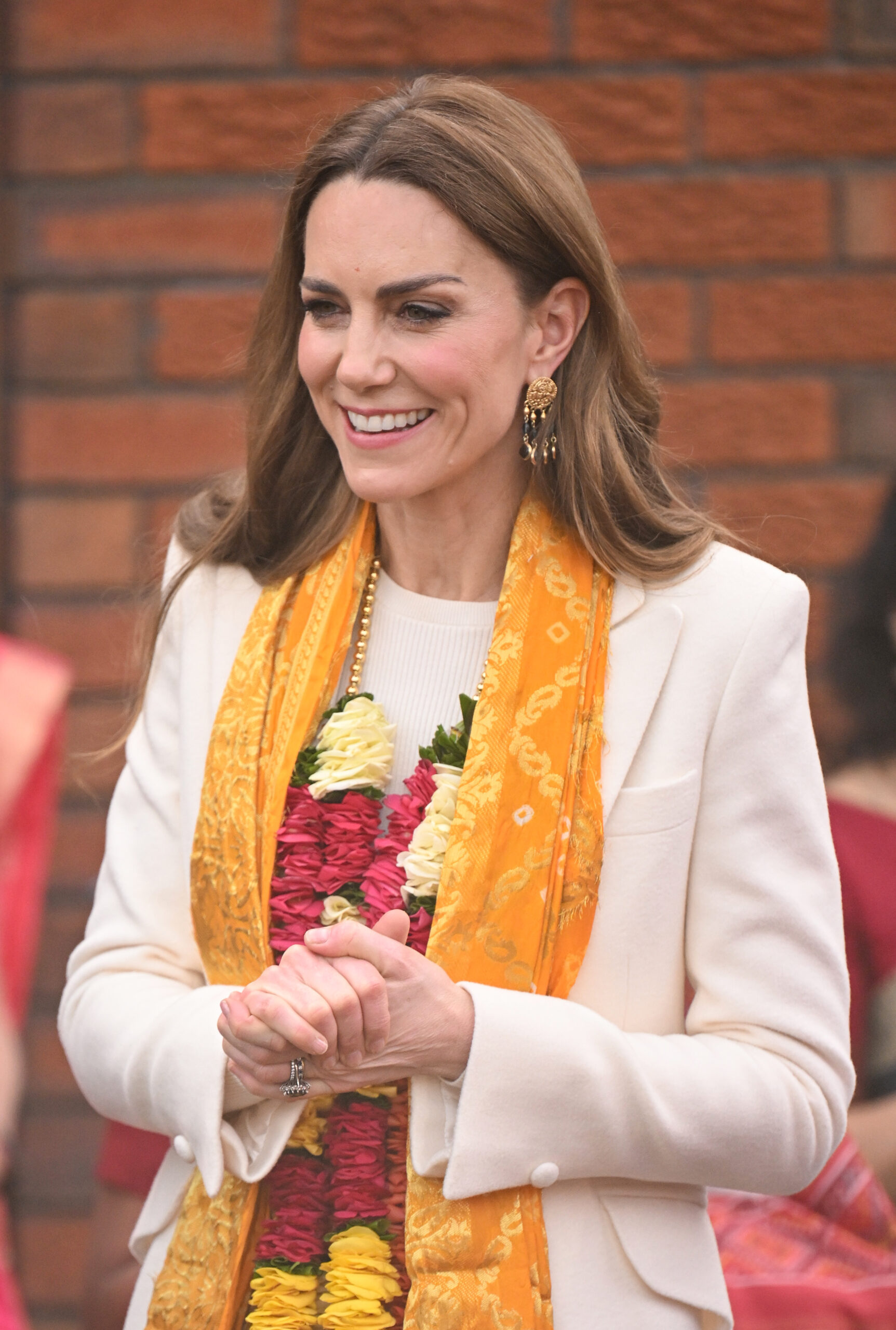 Princess Kate smiling wearing an orange and gold scarf and a garland