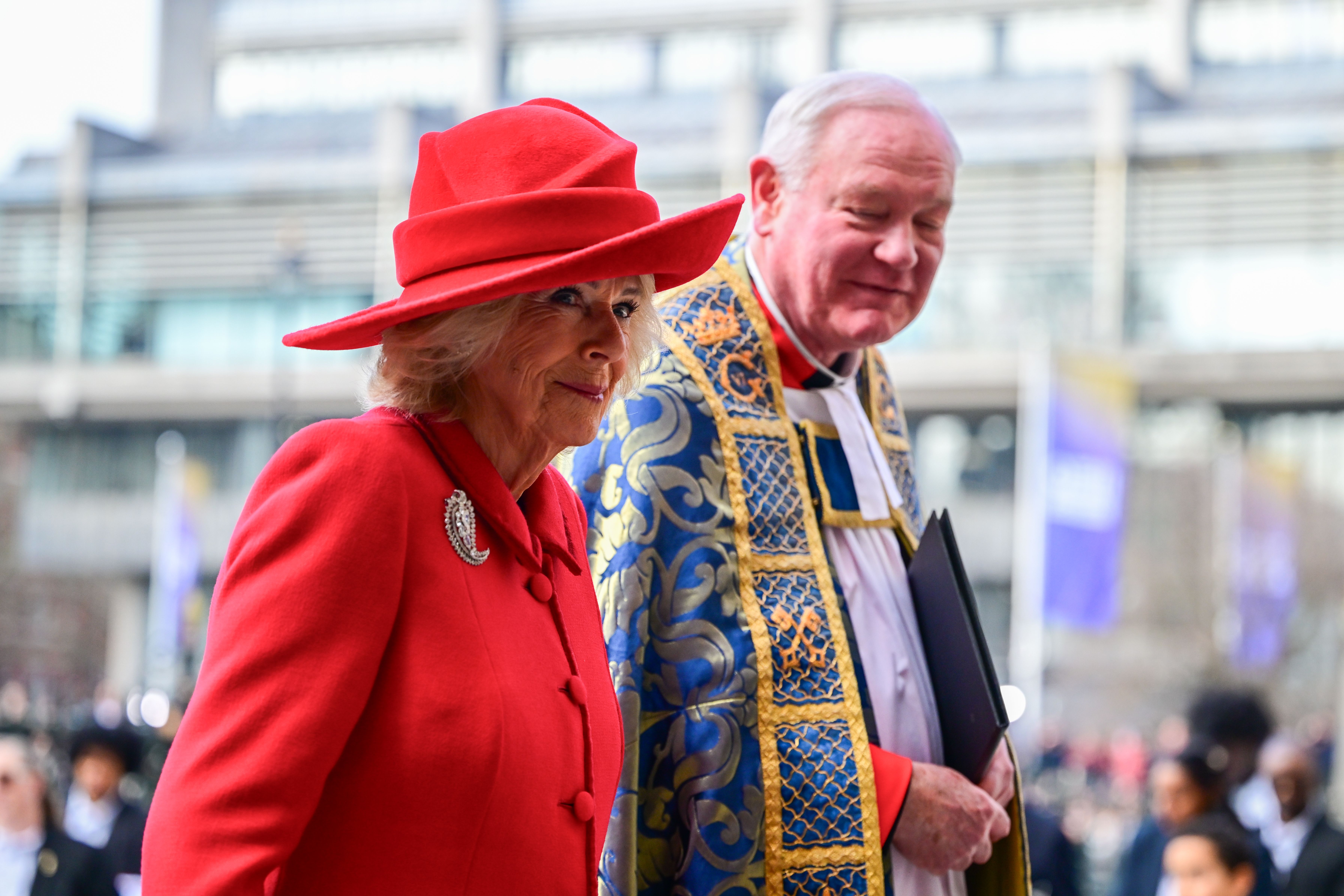 Queen Camilla up close wearing a red ensemble and leaf shaped brooch