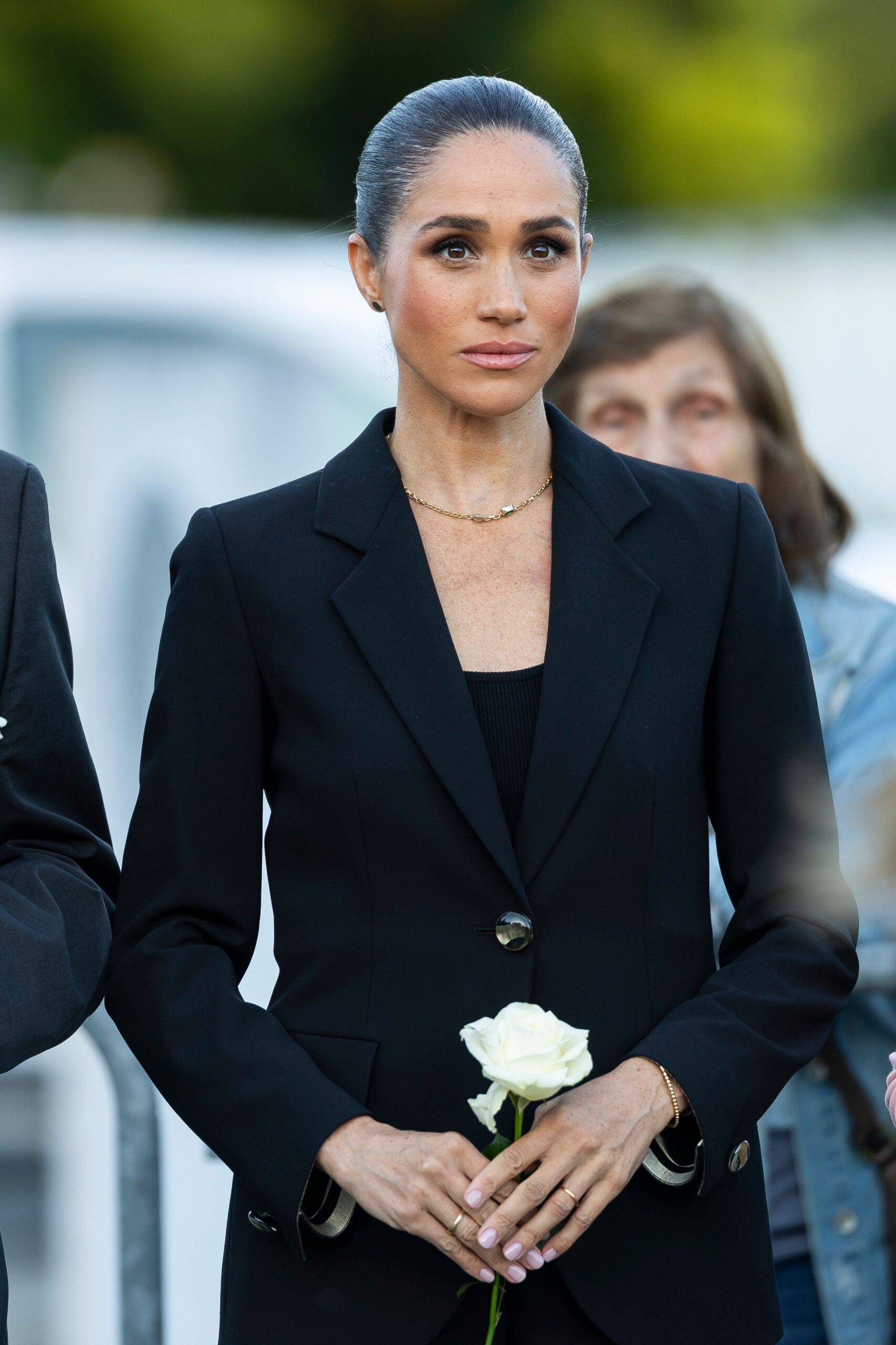 Meghan Markle holding a white rose with a sad expression